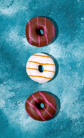 Donuts with white and chocolate icing on a blue background. Vertical photo