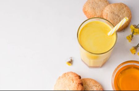 latte made of milk and turmeric on a white background. next to golden milk are honey and cookies. There is a place for copy space. Indian drinkの写真素材
