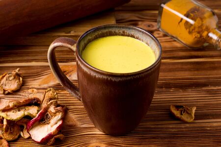 Indian drink golden milk on a wooden background next to fruit apple chips. rusticの写真素材