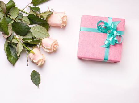 A gift in pink packaging on a white background next to a bouquet of white roses. there is a place for copy spaceの写真素材