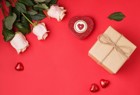 Valentine's Day gifts on a red background next to burning candles, heart-shaped sweets, white roses. copy space.の写真素材