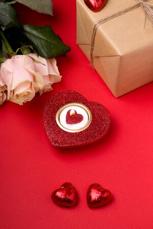 Valentine's Day gifts on a red background next to heart-shaped candles, flowers and, chocolate bars and craft paper gifts. Vertical imageの写真素材