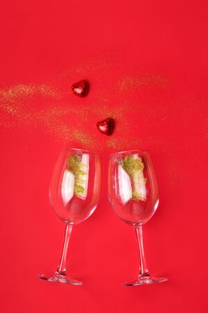 Glasses with golden sparkles and candy in the shape of hearts on a red background with copy space.の写真素材