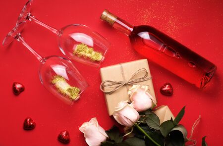 holiday concert with wine, gifts from craft paper, sweets and flowers on a red background. Suitable for Women's Day or Valentine's Dayの写真素材