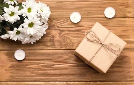 a gift on a wooden table next to candles and a bouquet of daisies. Valentine's day conceptの写真素材