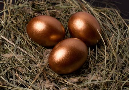 copper colored easter eggs on a black background in a nest of hay close-up.の写真素材
