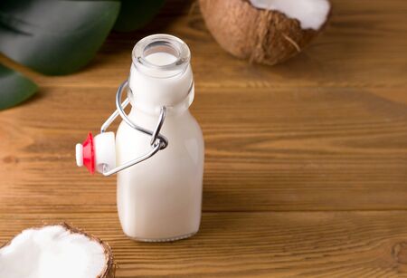 coconut milk on a wooden background in a glass bottle on a wooden background next to coconut halvesの写真素材