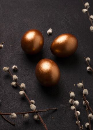 Copper-colored Easter eggs on a black background close-up next to willow branches. Vertical imageの写真素材