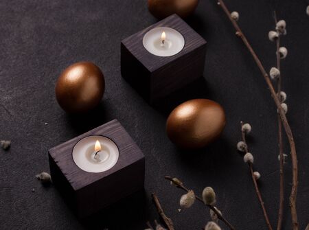copper colored easter eggs on a black background next to willow branches and candles close-upの写真素材