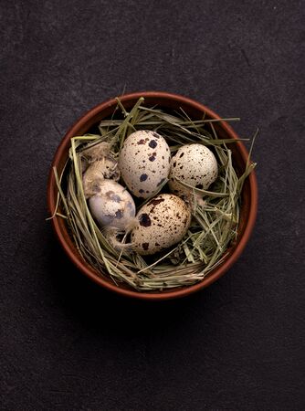 quail easter eggs on a black background in a clay bowl with hay.の写真素材