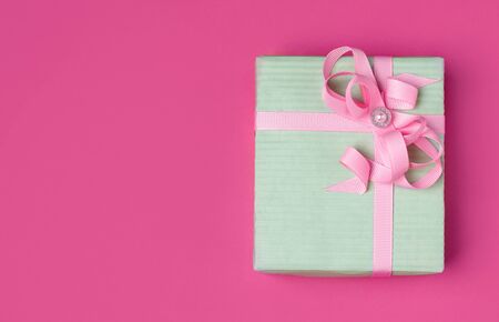 gift in a mint-colored wrapper with a pink ribbon on a pink background with copy space.の写真素材