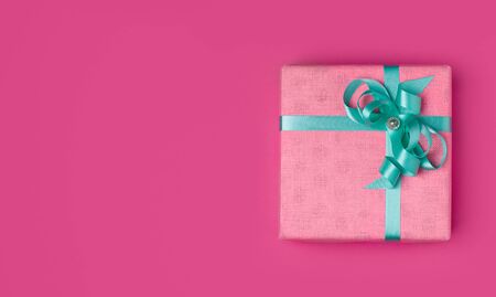 Pink gift with a turquoise ribbon on a pink background with place for copy space. The concept of the holiday of March 8, Valentine's day or birthday.の写真素材