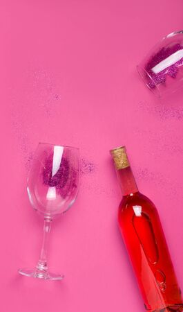 Vertical image with copy space, a bottle of wine and two glasses with sparkles on a pink background. The concept of holidays, Women's Day, Valentine's Day, Christmas, birthdayの写真素材
