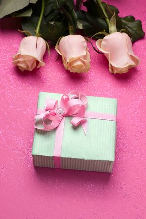 gift in mint packing on a pink background with flowers. Vertical image. The concept of a birthday holiday, women's day.の写真素材
