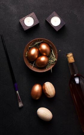 Easter eggs from a tree on a black background next to wine. concept of painting eggs in copper color for the Easter holidayの写真素材