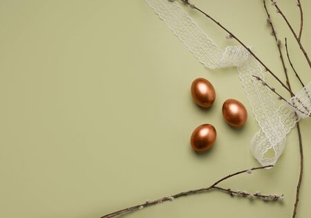 Copper-colored Easter eggs on a pale green background next to willow branches. There is copy space....