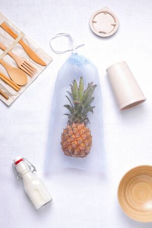 eco bag of blue color with tropical pineapple fruit on a white background next to environmentally friendly cutlery made of bambooの写真素材