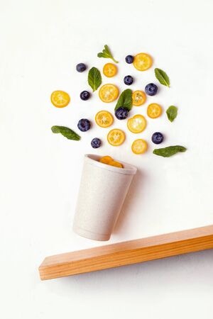 Reusable cup on a white background with flying blueberries and slices of kumquat. zero waste conceptの写真素材