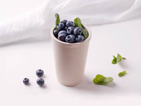 Reusable cup with blueberries and mint leaves on a light backgroundの写真素材