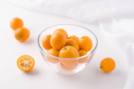 tropical kumquat fruit in a glass transparent bowl on a white background next to a clothの写真素材