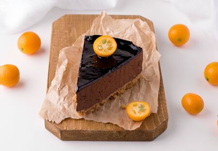 chocolate cake with cocoa on a wooden board decorated with citrus fruit kumquat on a white background. next to the dessert are fresh fruitsの写真素材
