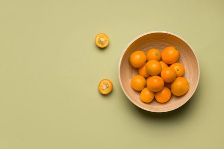 tropical citrus kumquat fruit in a bamboo bowl on a green background. copy spaceの写真素材