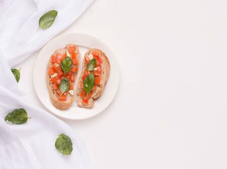 Bruschetta is a traditional Italian dish with tomato, garlic on a plate next to a cloth and basil leaves. copy spaceの写真素材