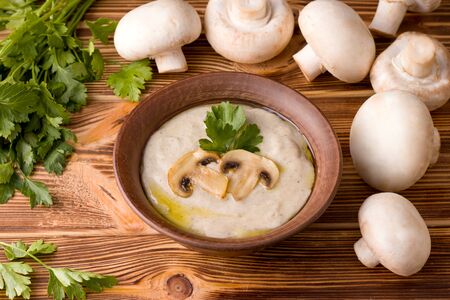 mushroom cream soup is a traditional European dish on a wooden table next to the ingredients fresh champignons and herbs.の写真素材