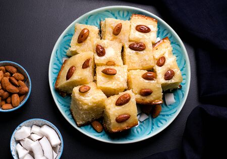 oriental confectionery based on semolina arabic Busbus pie poured with syrup in a blue plate on a black background close-up.の写真素材