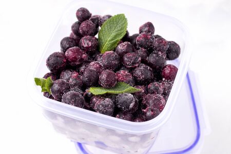 frozen blackcurrant berries on a white plate in a glass containerの写真素材