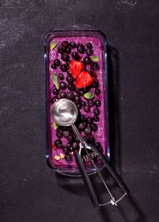 ube and blackcurrant sorbet decorated with strawberry slices on a black backgroundの写真素材