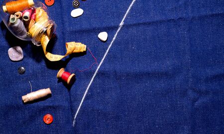 The concept of sewing at home. Jar of thread and buttons on a blue denim. Copy space.の写真素材