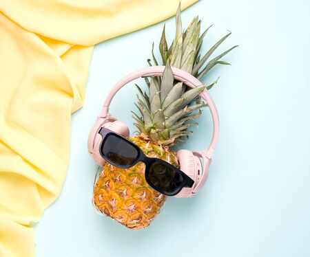 Summer concept with tropical pineapple fruit in sunglasses and headphones on a blue background.の写真素材