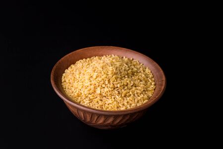 Raw bulgur groats on a black background in a traditional bowlの写真素材