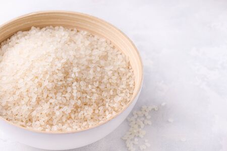 Raw uncooked rice close-up in a bowl on a white background. Copy spaceの写真素材