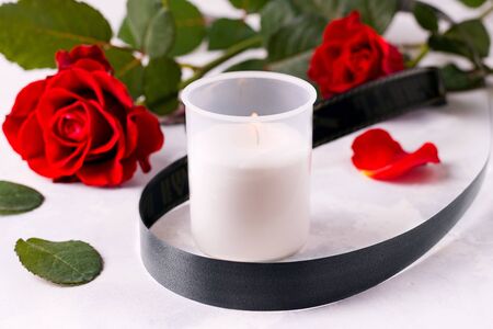 A candle with a black mourning ribbon on a white background next to red roses. The concept of loss, sorrow and deathの写真素材