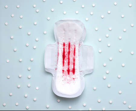 PMS pain treatment concept. pad on blue background next to pills