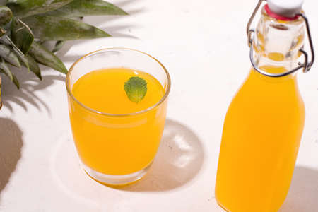 Fermented kombucha pineapple summer drink in a glass and a bottle on a white backgroundの写真素材