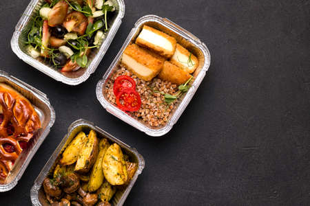 Home delivery concept. On a black background porridge with vegetables, potatoes and mushrooms, salad. Copy spaceの写真素材