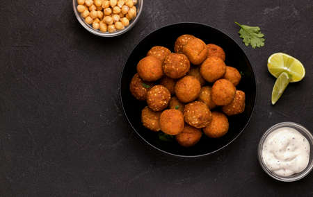 Falafel dish of chopped legumes, seasoned with spices on a black background with sauce and lime. Copy spaceの写真素材