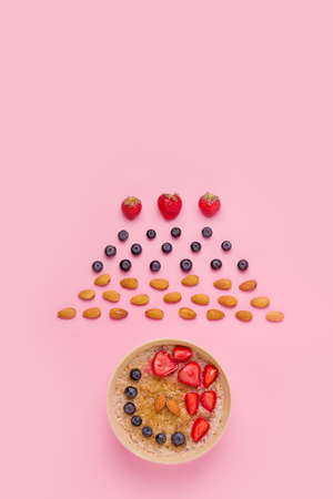 Breakfast of porridge with fresh berries and almonds on a pink background. Copy spaceの写真素材