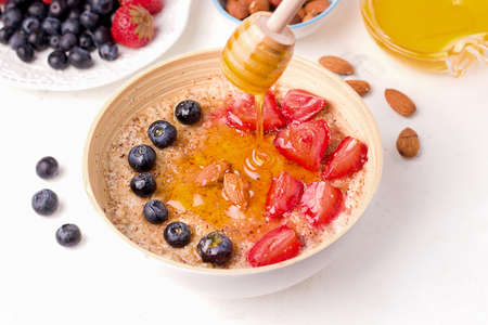 Healthy summer breakfast. Oatmeal porridge with fresh berries, almonds and honey on a white plateの写真素材