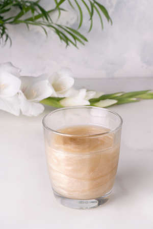 drink with shimmer in a glass on a gray background next to white flowersの写真素材