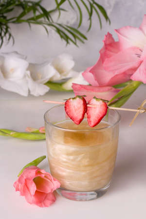 A drink with a shiny shimmer decorated with strawberry wedges next to flowersの写真素材