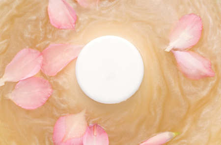 Mockup of cosmetic products. White round jar on water with shimmer and flower petalsの写真素材