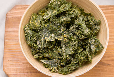 Kale chips close-up in a bowl on a wooden boardの写真素材