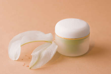 Cosmetics concept. Round jar for cream on a brown background next to the petals of a white flowerの写真素材
