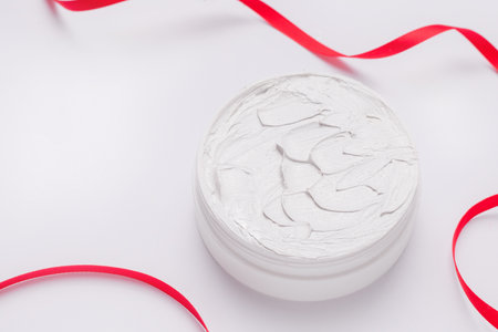 Gift cosmetics concept. Cream in a jar on a white background with a red ribbon. Copy spaceの写真素材