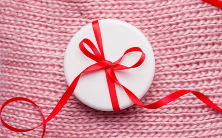 Gift Christmas cosmetics concept. Cream in a white jar on the texture of a knitted pink scarf. View from aboveの写真素材