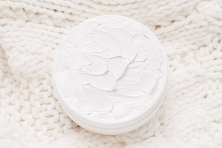 Winter face and body care concept. Organic cream on a knitted white sweater. View from aboveの写真素材